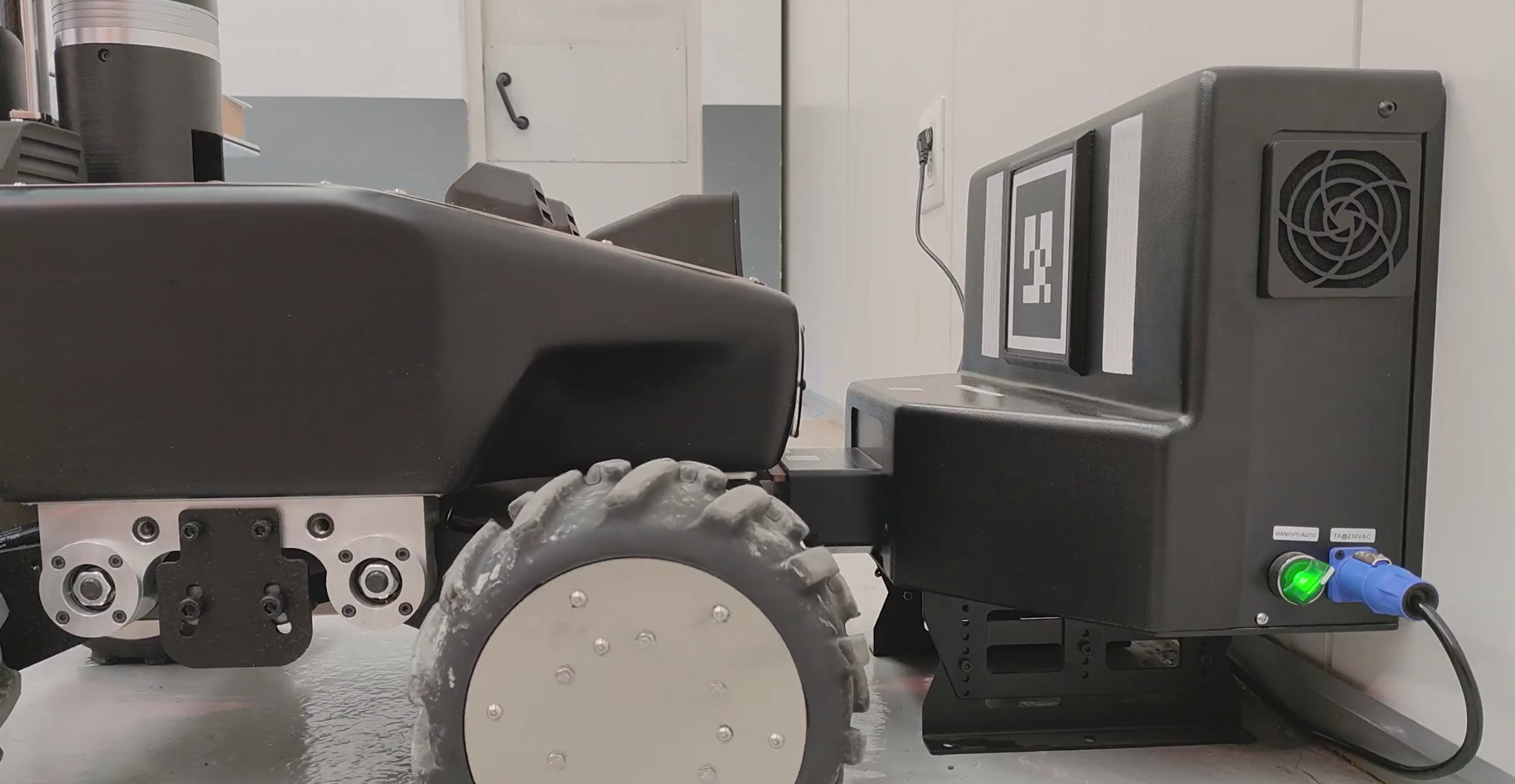 Robot E-Sentinel positionné devant sa station de charge, avec les connecteurs et le voyant de la borne visibles.